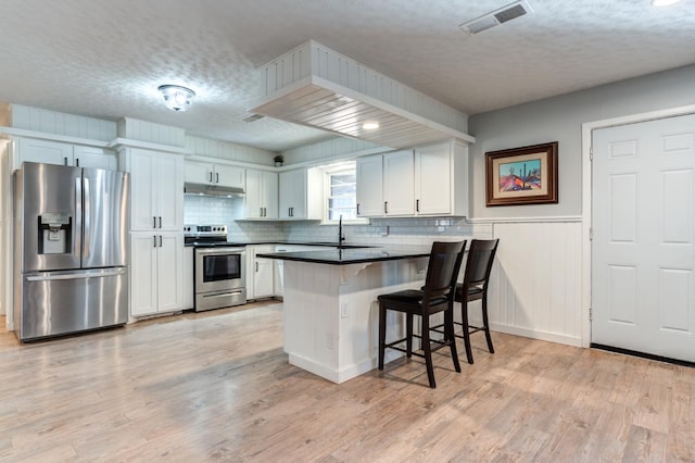 kitchen featuring light hardwood / wood-style flooring, appliances with stainless steel finishes, a kitchen breakfast bar, kitchen peninsula, and white cabinets