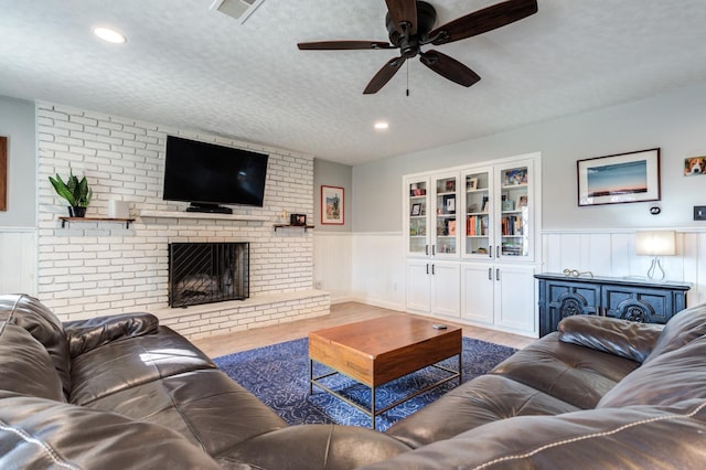 living room featuring ceiling fan, a brick fireplace, hardwood / wood-style floors, and a textured ceiling