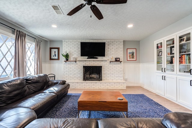 living room with built in shelves, a textured ceiling, ceiling fan, a fireplace, and light hardwood / wood-style floors