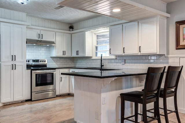 kitchen featuring sink, white cabinetry, a kitchen breakfast bar, stainless steel electric range oven, and kitchen peninsula