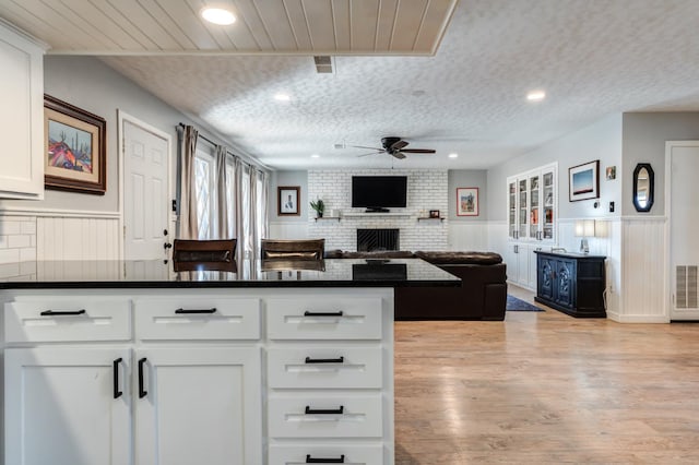 kitchen featuring white cabinets, ceiling fan, a brick fireplace, a textured ceiling, and light wood-type flooring