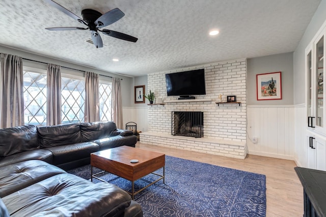 living room featuring ceiling fan, a textured ceiling, light wood-type flooring, and a fireplace