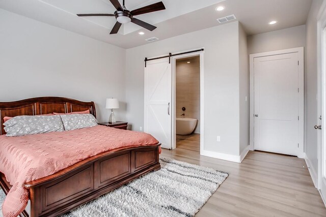 bedroom with ensuite bathroom, a barn door, ceiling fan, and light wood-type flooring