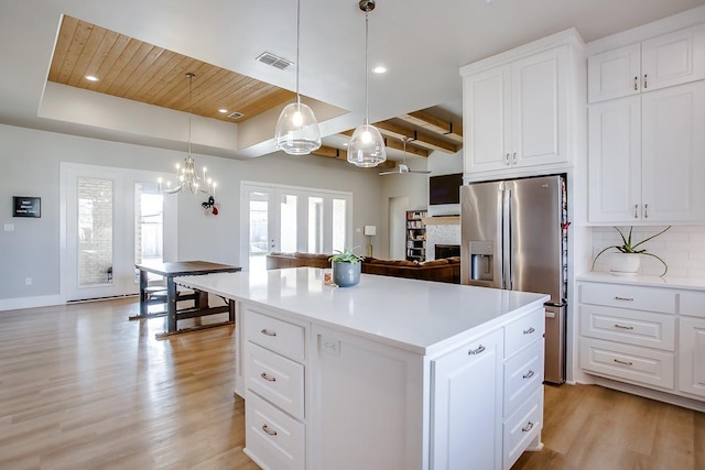 kitchen with a center island, stainless steel fridge with ice dispenser, a raised ceiling, pendant lighting, and white cabinets