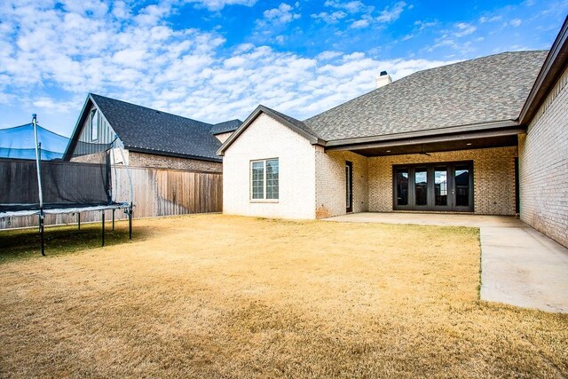 back of house with a trampoline, a patio area, french doors, and a lawn