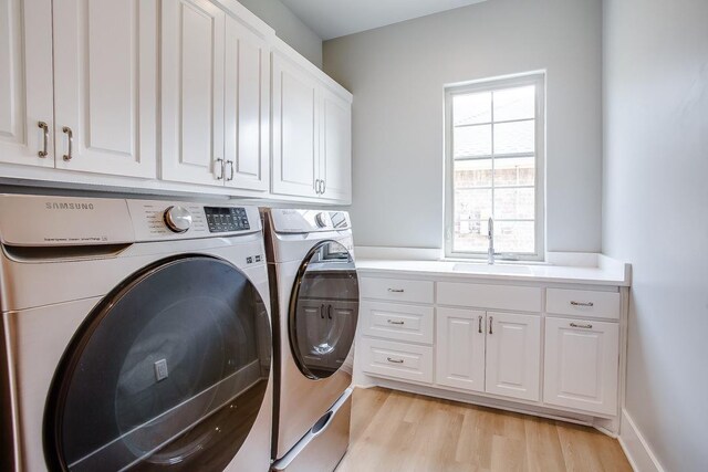 clothes washing area featuring separate washer and dryer, sink, cabinets, and light wood-type flooring