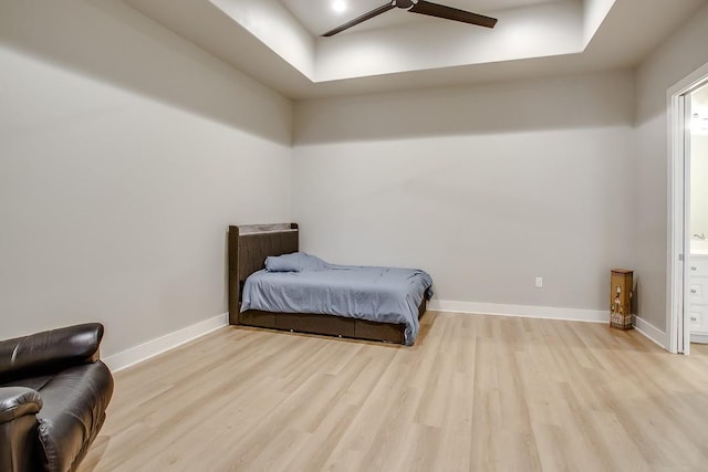 bedroom featuring connected bathroom, a tray ceiling, and light wood-type flooring