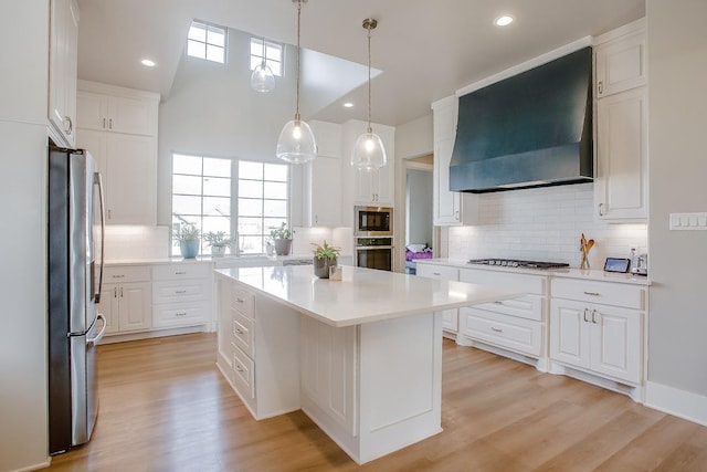 kitchen featuring appliances with stainless steel finishes, premium range hood, a center island, white cabinets, and decorative light fixtures