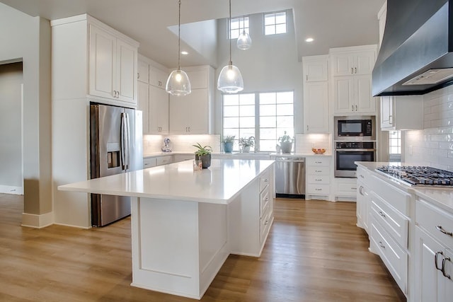 kitchen featuring white cabinetry, hanging light fixtures, appliances with stainless steel finishes, a kitchen island, and range hood