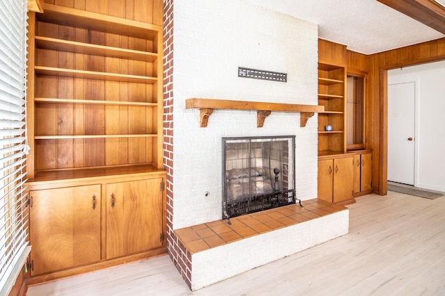 unfurnished living room featuring a large fireplace, built in features, wooden walls, and light hardwood / wood-style flooring