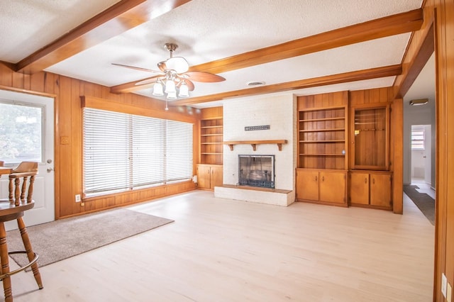 unfurnished living room with light hardwood / wood-style floors, a textured ceiling, a brick fireplace, beamed ceiling, and wood walls