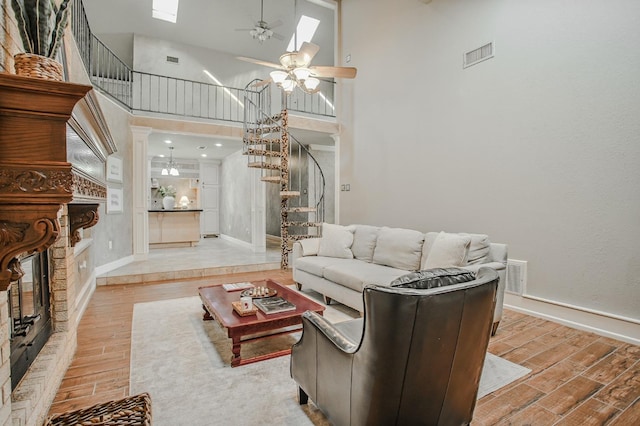 living room with a stone fireplace, light hardwood / wood-style floors, ceiling fan, and a high ceiling