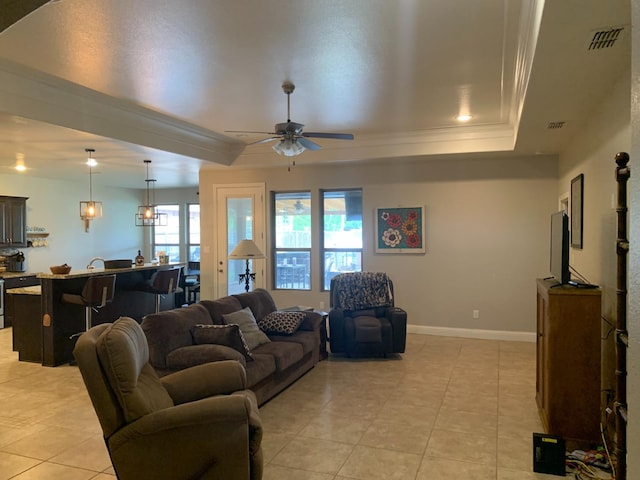 tiled living room with crown molding, ceiling fan, and a raised ceiling