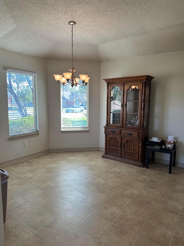 unfurnished dining area featuring a textured ceiling and a chandelier