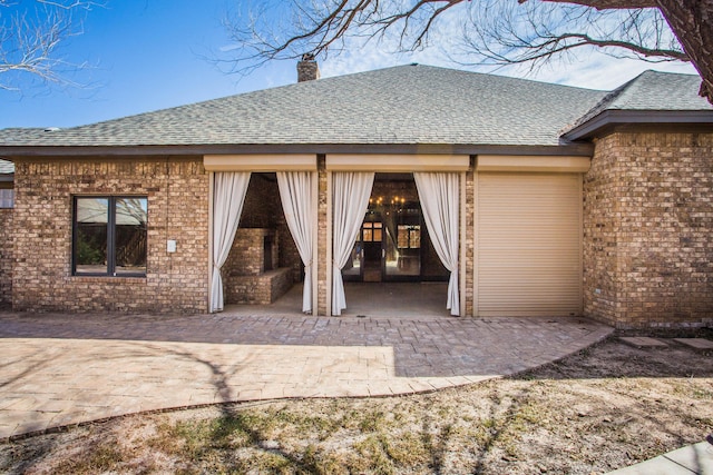 back of house featuring a shingled roof, a chimney, a patio, and brick siding