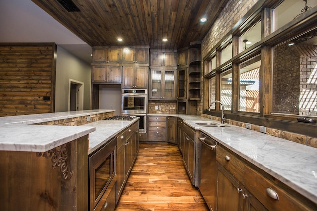 kitchen featuring appliances with stainless steel finishes, glass insert cabinets, a sink, and dark brown cabinetry