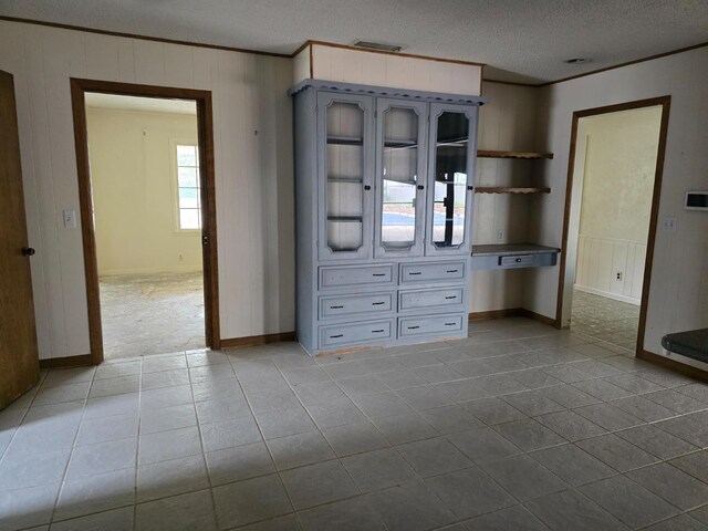 unfurnished bedroom featuring crown molding, wooden walls, light tile patterned floors, and a textured ceiling