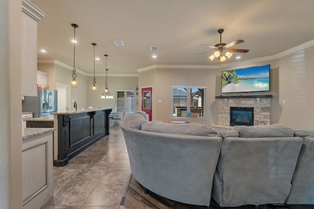 tiled living room featuring ceiling fan, ornamental molding, and a stone fireplace