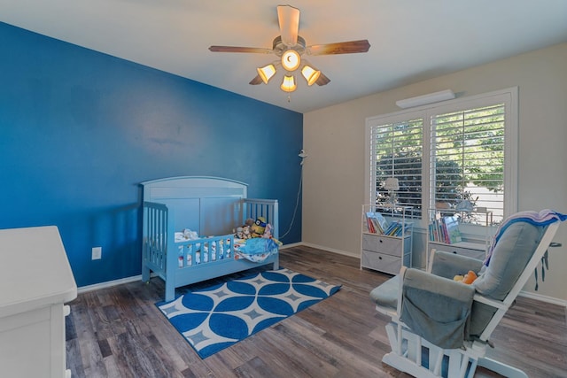 bedroom featuring a nursery area, dark hardwood / wood-style floors, and ceiling fan