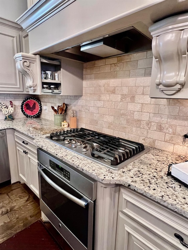 kitchen with appliances with stainless steel finishes, white cabinets, light stone counters, and decorative backsplash