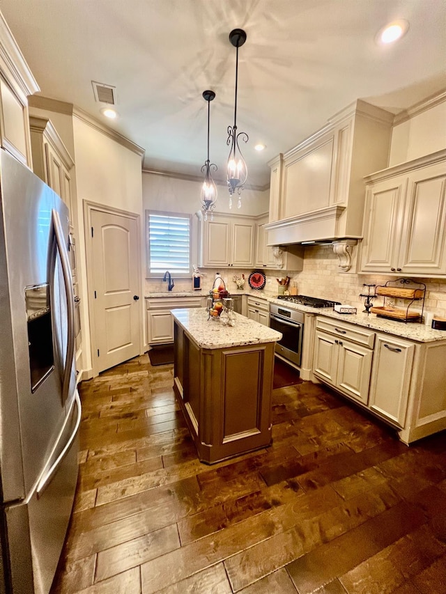 kitchen featuring light stone counters, appliances with stainless steel finishes, decorative light fixtures, and a center island