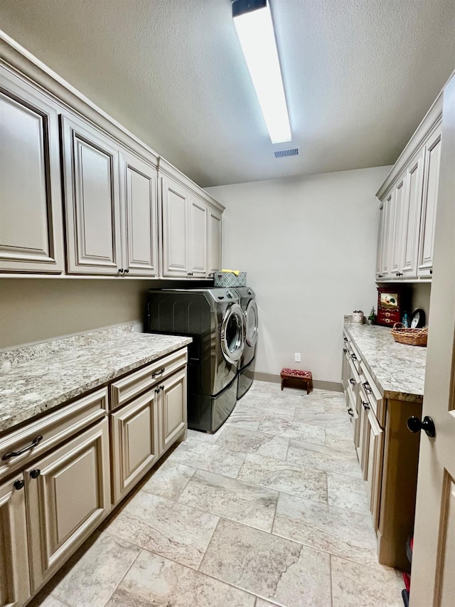 washroom featuring cabinets, a textured ceiling, and washing machine and clothes dryer