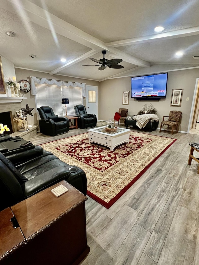 living area featuring a fireplace with raised hearth, ceiling fan, ornamental molding, wood finished floors, and beamed ceiling