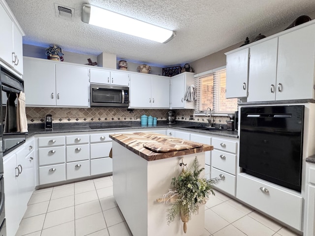 kitchen with black electric stovetop, light tile patterned floors, stainless steel microwave, and a sink