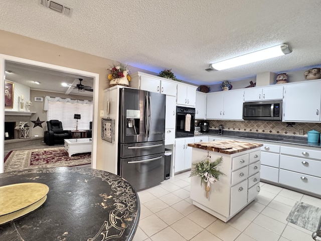 kitchen with light tile patterned floors, a fireplace, visible vents, white cabinets, and black appliances