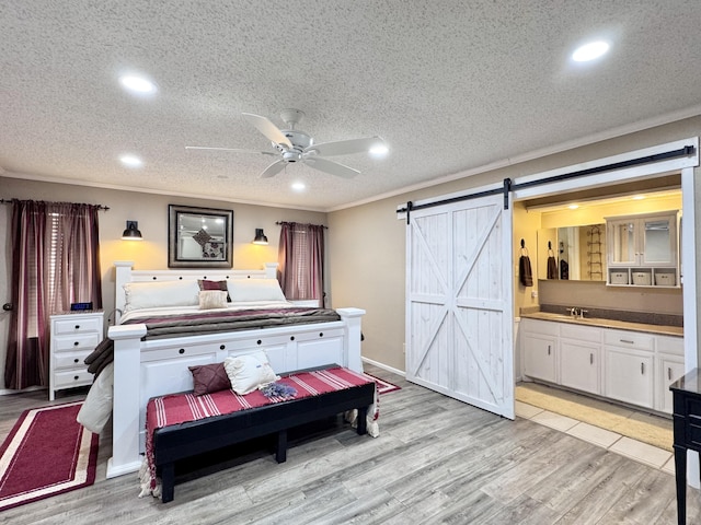 bedroom with light wood-style floors, a barn door, ornamental molding, and a textured ceiling