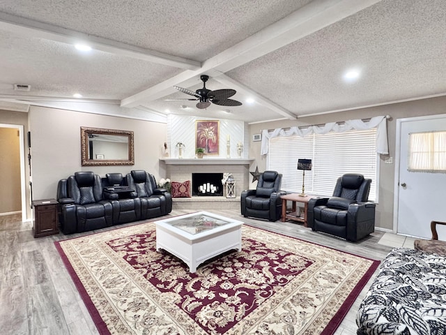 living area featuring light wood-style flooring, a textured ceiling, a fireplace with raised hearth, and beamed ceiling