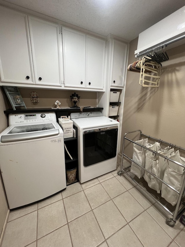 washroom with washer and dryer, cabinet space, a textured ceiling, and light tile patterned flooring