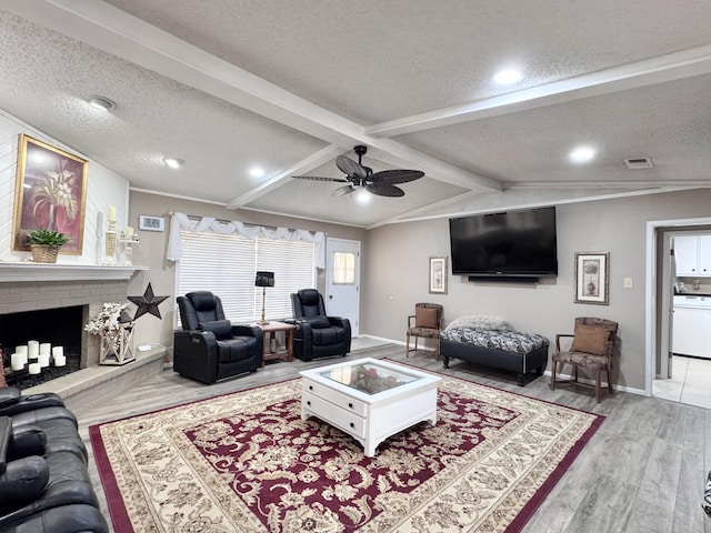 living room featuring a textured ceiling, lofted ceiling with beams, a brick fireplace, and visible vents