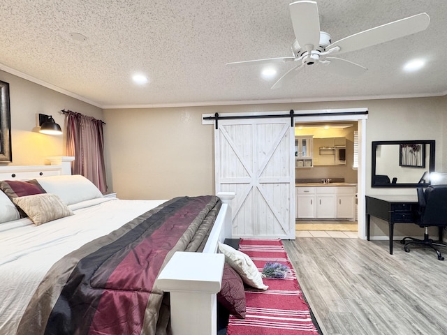 bedroom featuring a textured ceiling, a barn door, connected bathroom, light wood-style floors, and crown molding