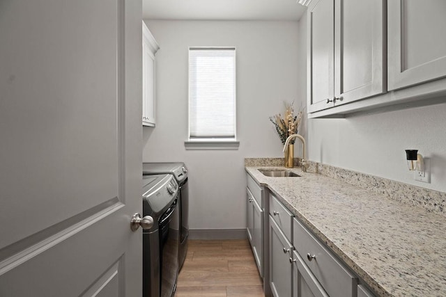 washroom featuring baseboards, light wood finished floors, cabinet space, a sink, and washer and dryer