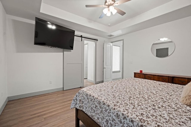 bedroom with visible vents, baseboards, light wood-type flooring, a barn door, and a raised ceiling