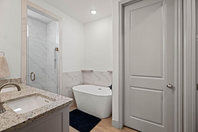 full bath with wood finished floors, tile walls, a shower stall, a soaking tub, and vanity