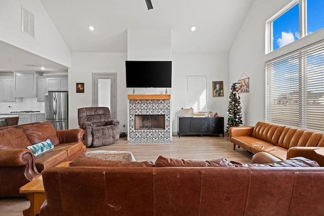 living area with a fireplace, visible vents, light wood finished floors, and high vaulted ceiling