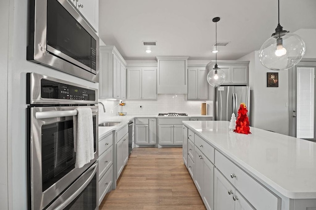 kitchen with a sink, custom range hood, appliances with stainless steel finishes, backsplash, and a center island