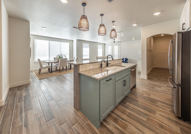 kitchen with arched walkways, stainless steel appliances, wood finish floors, and a sink