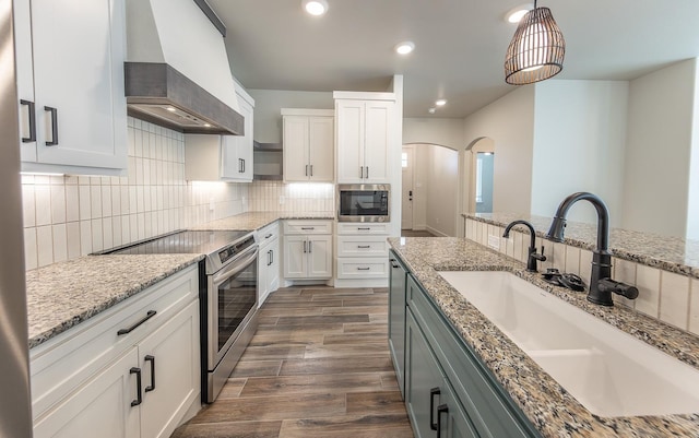 kitchen with arched walkways, a sink, decorative backsplash, custom range hood, and appliances with stainless steel finishes