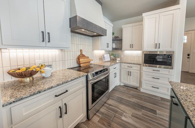 kitchen with premium range hood, wood finish floors, appliances with stainless steel finishes, white cabinetry, and backsplash