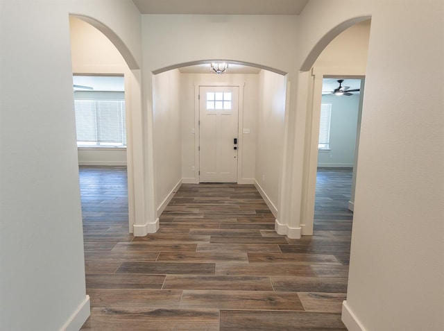 entrance foyer featuring arched walkways, baseboards, and dark wood-style flooring