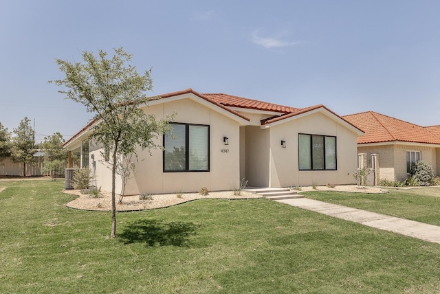 view of front facade featuring stucco siding, fence, a front lawn, and a tiled roof