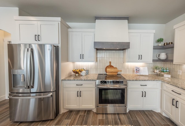 kitchen featuring open shelves, white cabinetry, appliances with stainless steel finishes, wall chimney range hood, and decorative backsplash