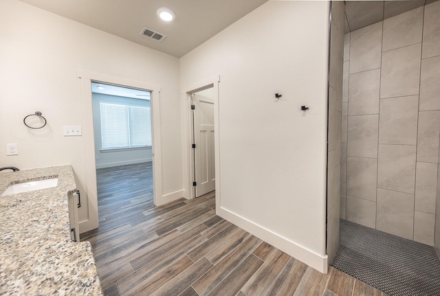 full bathroom with visible vents, wood tiled floor, tiled shower, baseboards, and vanity