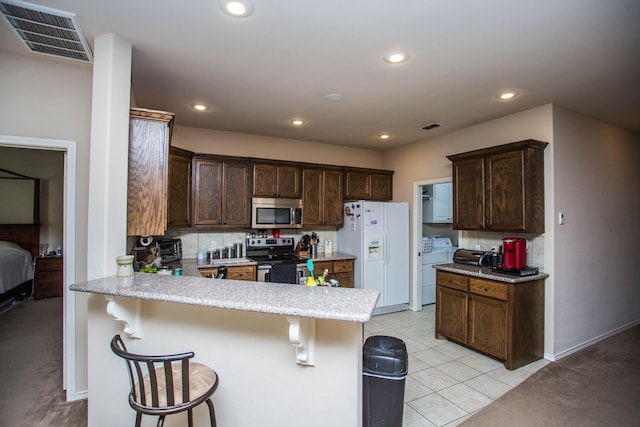 kitchen featuring appliances with stainless steel finishes, a breakfast bar, washing machine and clothes dryer, and kitchen peninsula