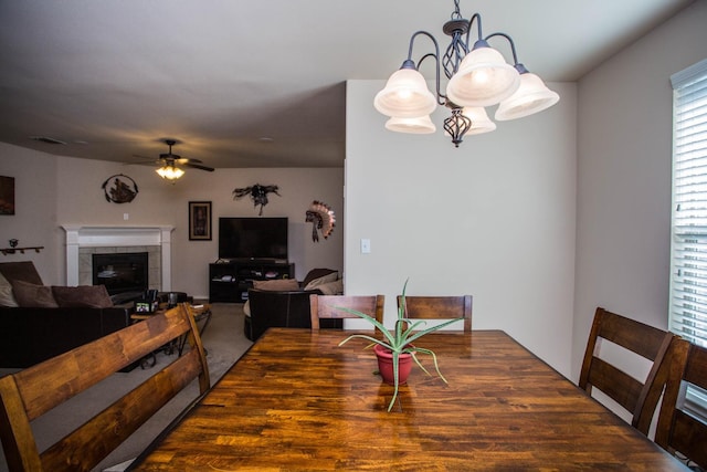 carpeted dining area with a fireplace and ceiling fan with notable chandelier