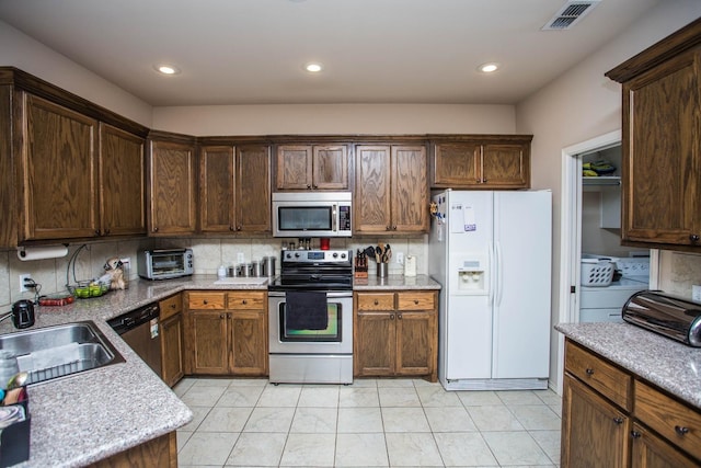 kitchen featuring sink, stainless steel appliances, independent washer and dryer, tasteful backsplash, and light stone countertops