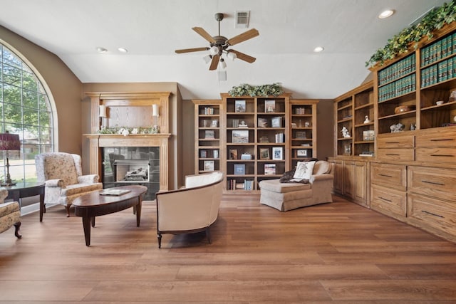 sitting room with lofted ceiling, a tile fireplace, ceiling fan, and light wood-type flooring